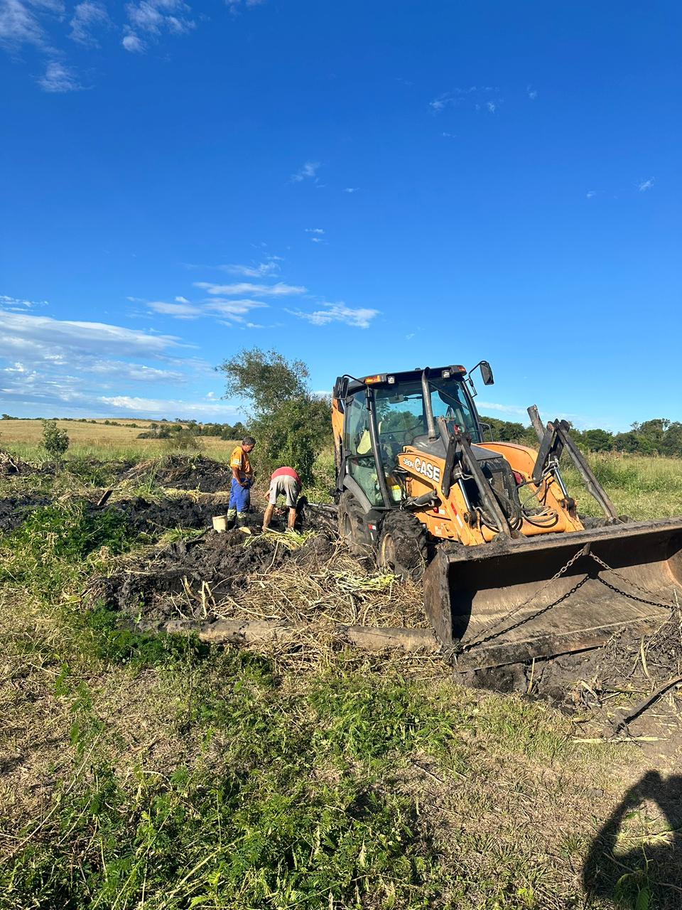 Limpeza de açude — equipe e retroescavadeira removendo vegetação e assoreamento